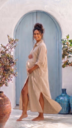 Woman in a beige dress standing in front of a blue door with decorative vases and plants.
